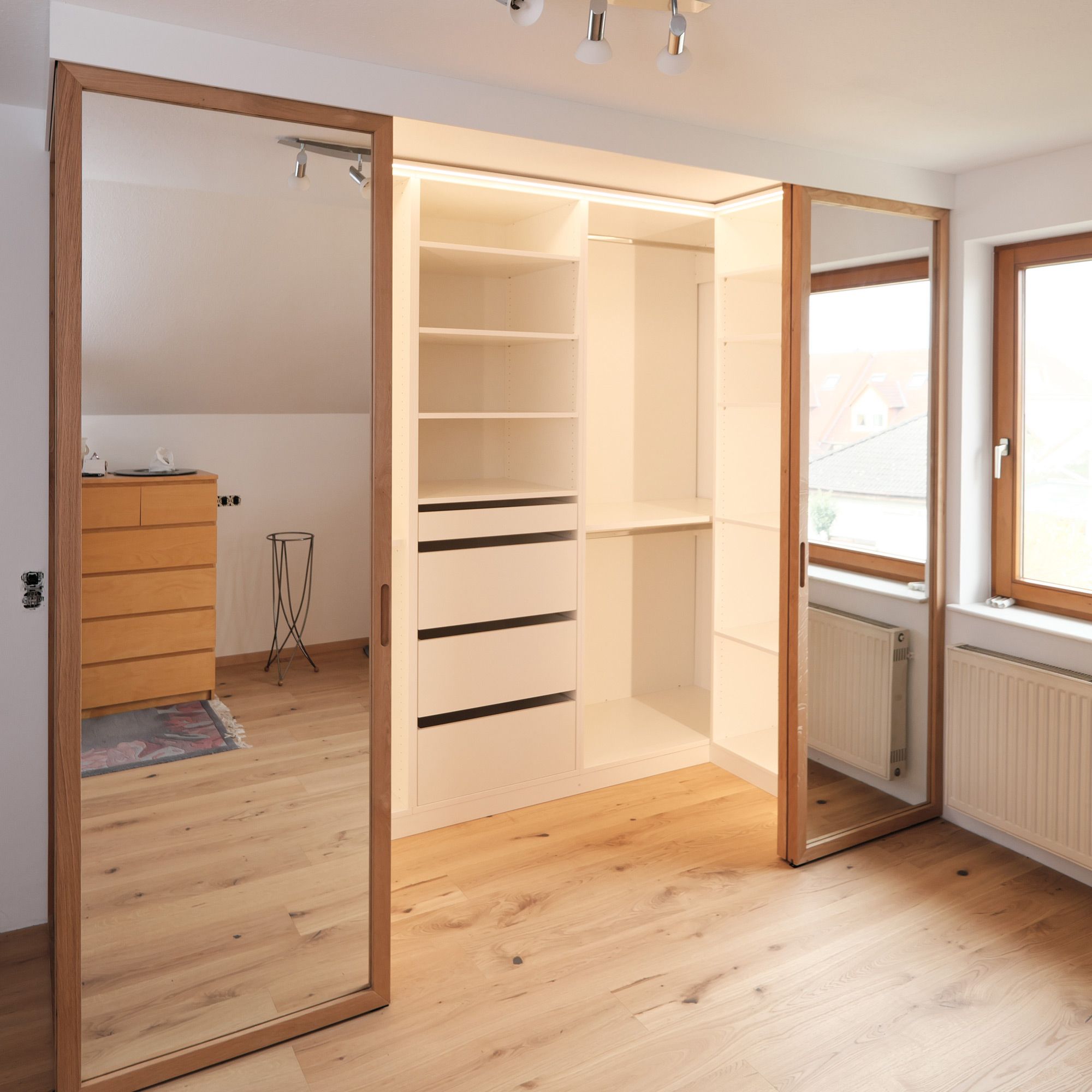 Begehbarer Kleiderschrank mit geöffneten Spiegel-Schiebetüren, LED-Licht und weißen Schubladen
