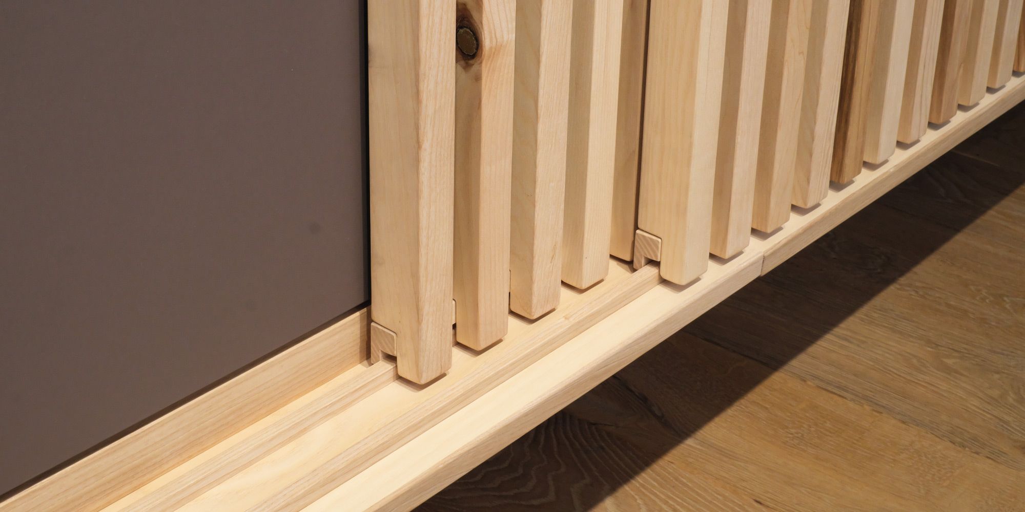 Detailaufnahme einer hellen Holz-Lamellenfront mit präziser Fräsung an der Sockelleiste