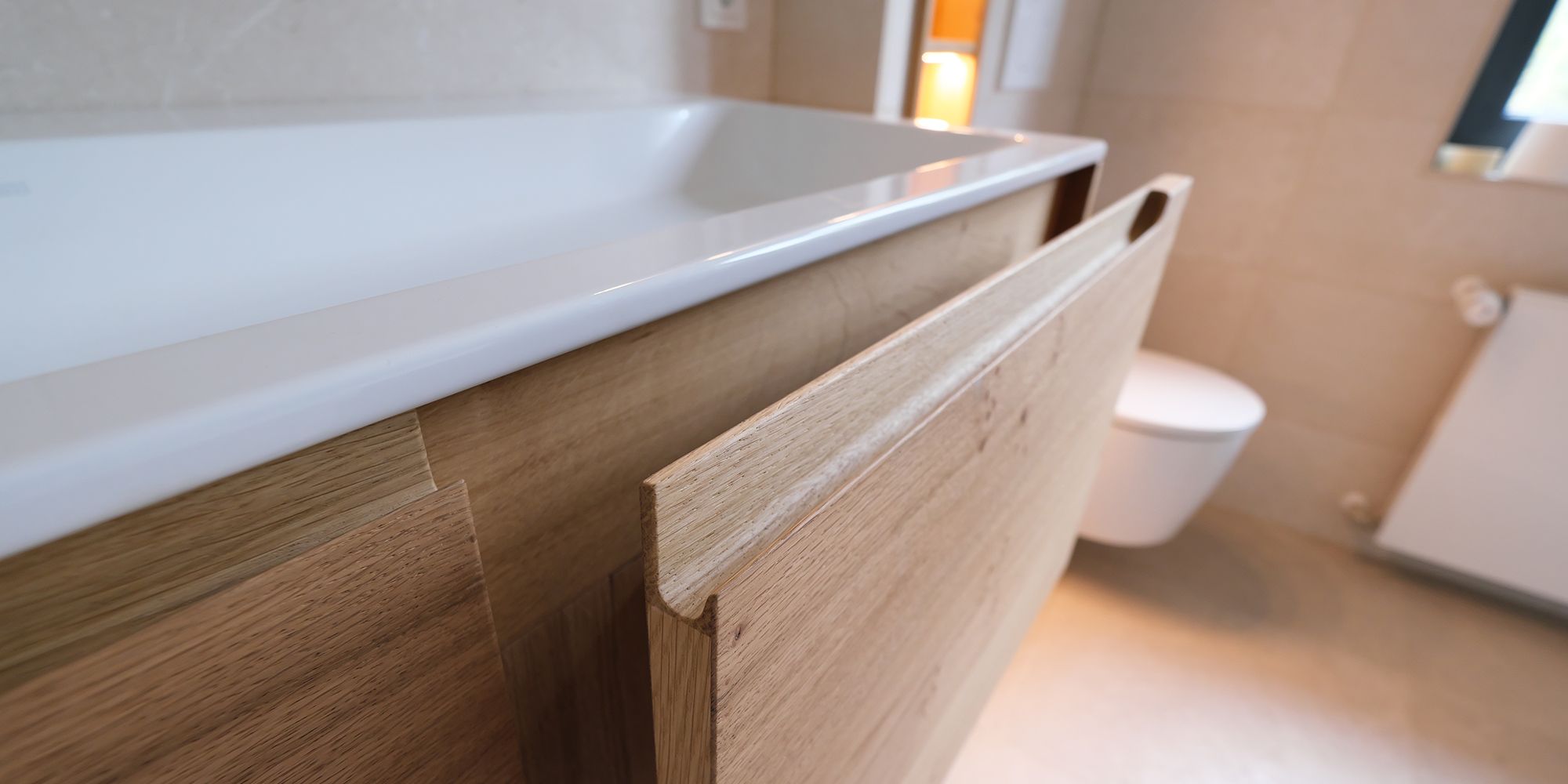 Offene Waschtisch-Tür aus Eiche mit integrierter Griffleiste neben Badewanne mit Mineralwerkstoff-Rand