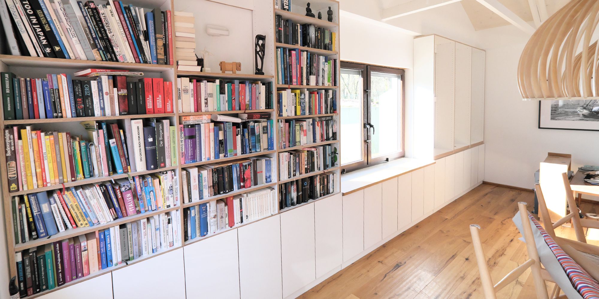 Raumhohes Bücherregal mit weißlackiertem Einbauschrank und Eiche-Fensterbank unter dem Dach