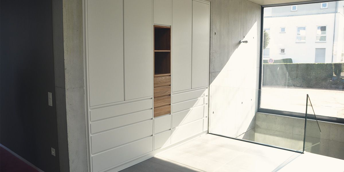 Weißer Einbauschrank mit offenem Nussbaum-Fach vor Sichtbetonwand in modernem Architektenhaus