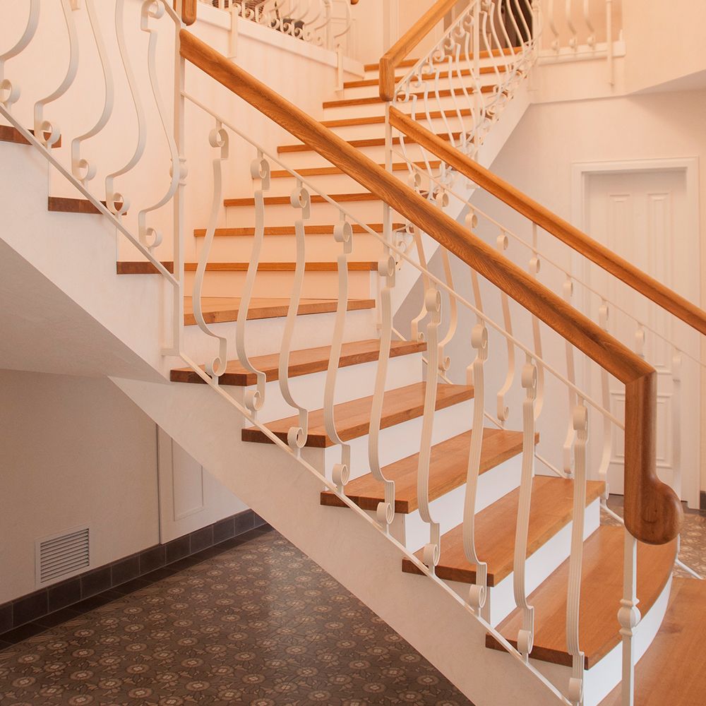 Geschwungene Treppe mit Eichenstufen und weißem Schmiedeeisen-Geländer im klassischen Eingangsbereich