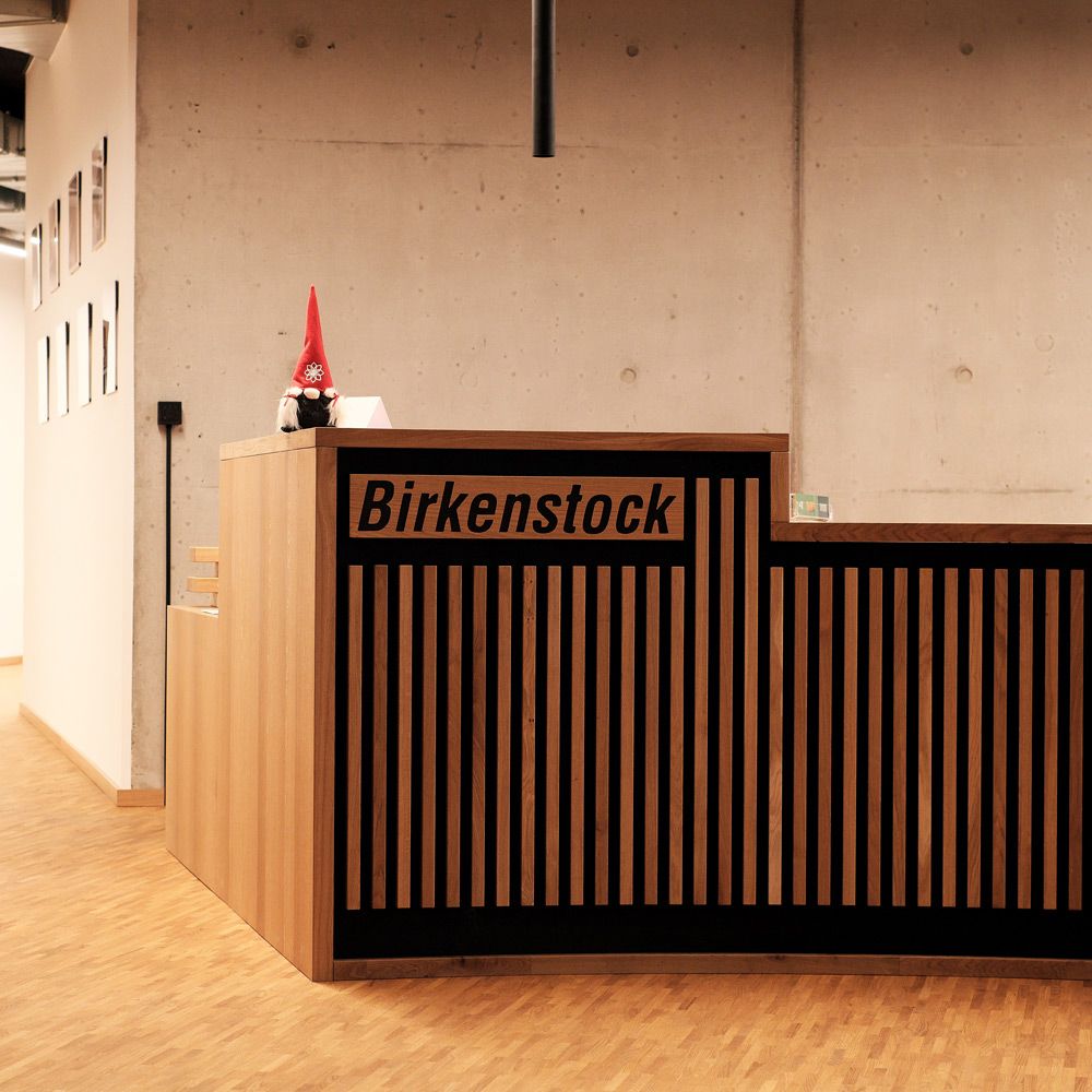 Empfangstheke aus Eichenlamellen mit eingefrästem Firmenlogo vor Sichtbetonwand