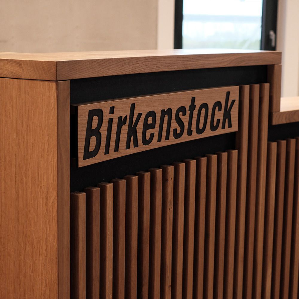 Nahaufnahme der Eichenlamellen mit gefrästem Birkenstock-Logo an der Empfangstheke