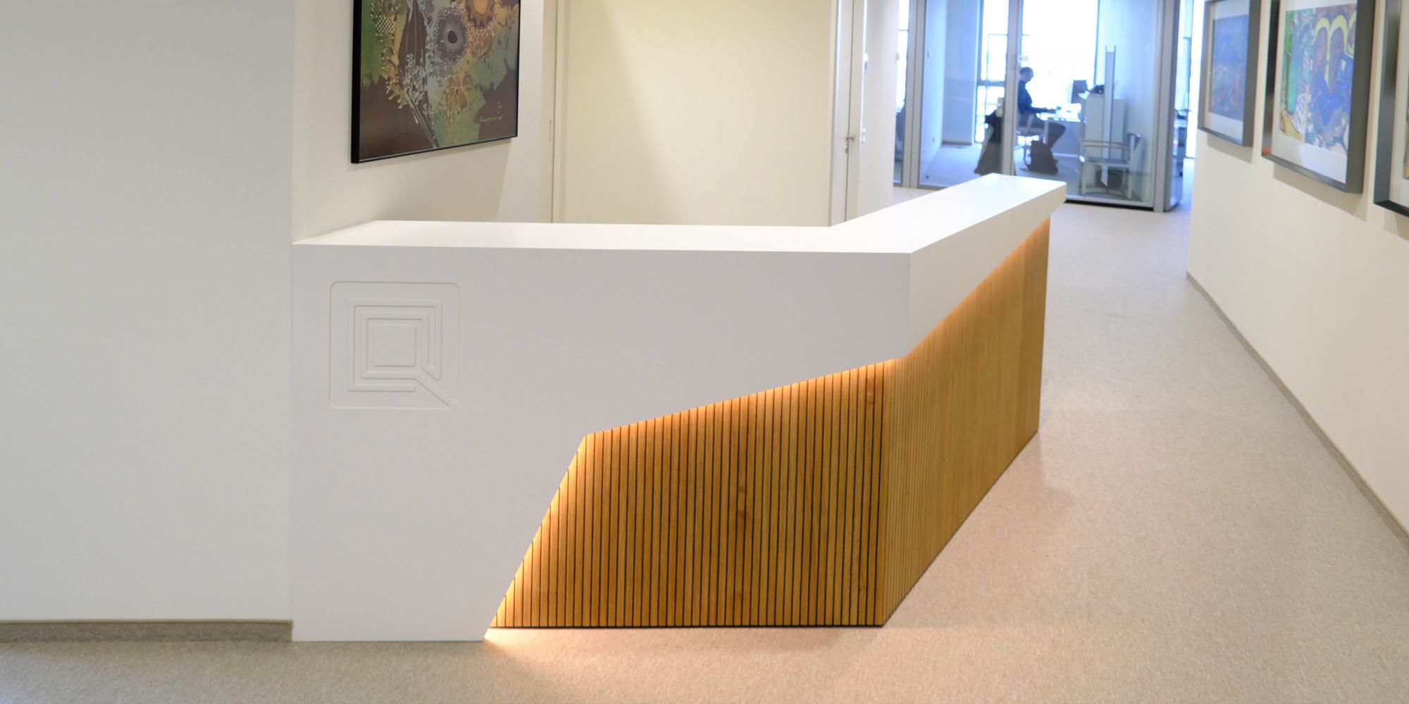Weiße Empfangstheke mit LED-hinterleuchteten Eichenlamellen im hellen Bürokorridor