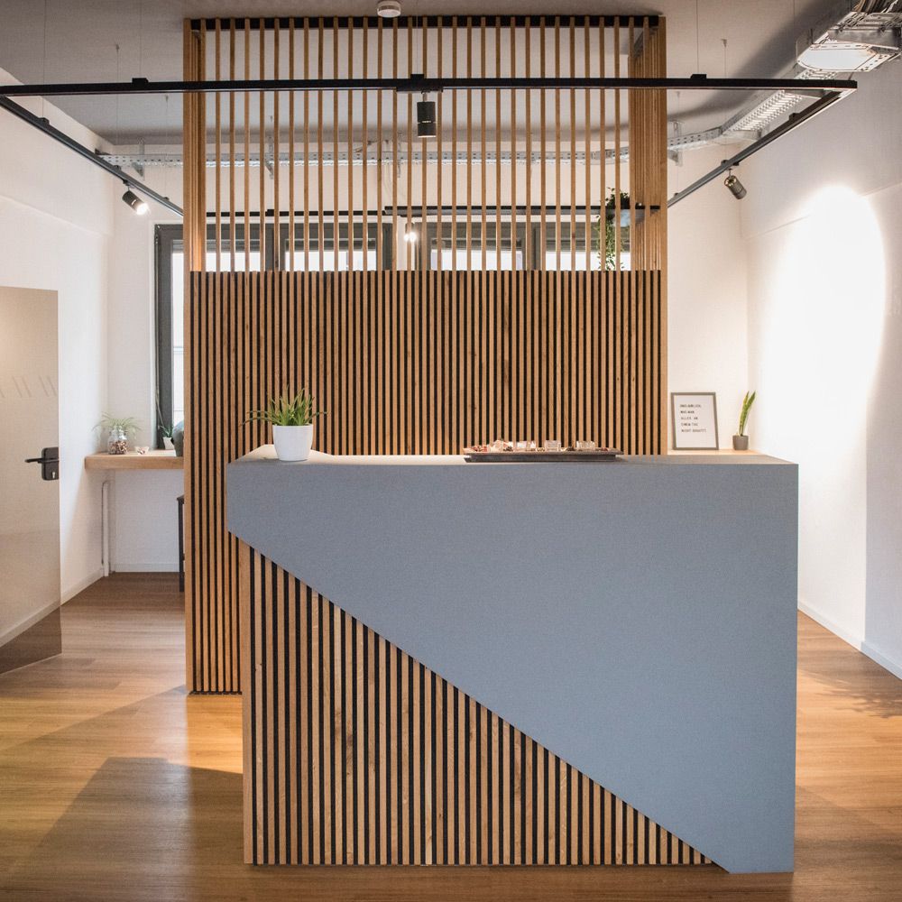 Empfangstheke mit Eichen-Holzlamellenwand und grauer Linoleum-Arbeitsplatte im diagonalen Design