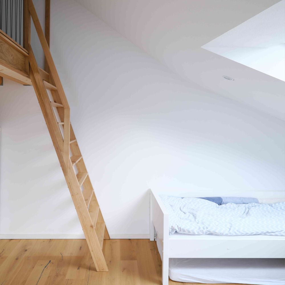 Steile Holztreppe zur Empore im Dachgeschoss-Kinderzimmer neben weißem Bett