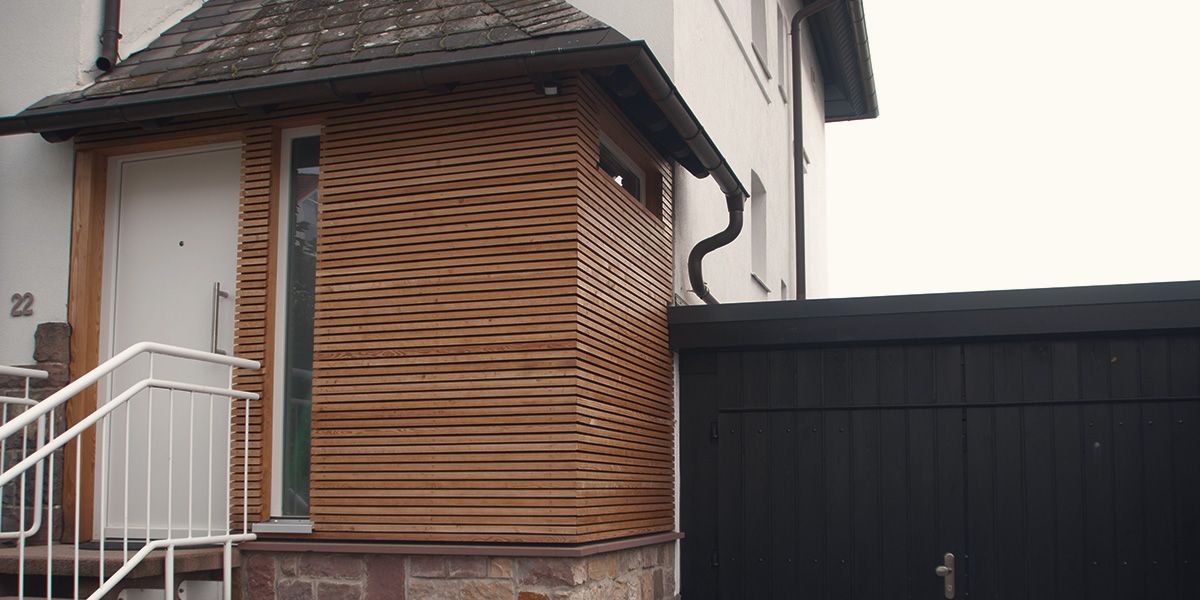 Moderne Hausfassade mit horizontaler Holzlattung neben Eingangstür und Steintreppe