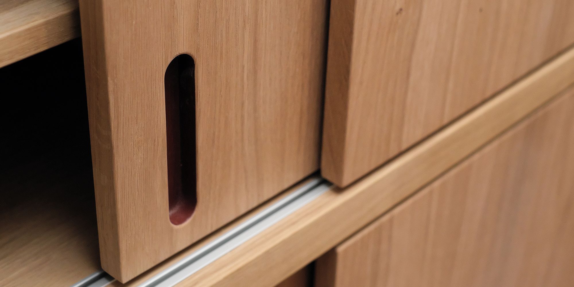 Griffmulde einer Eichen-Schiebetür an der Garderobe, innen rot lackiert, mit Aluminium-Führungsschiene