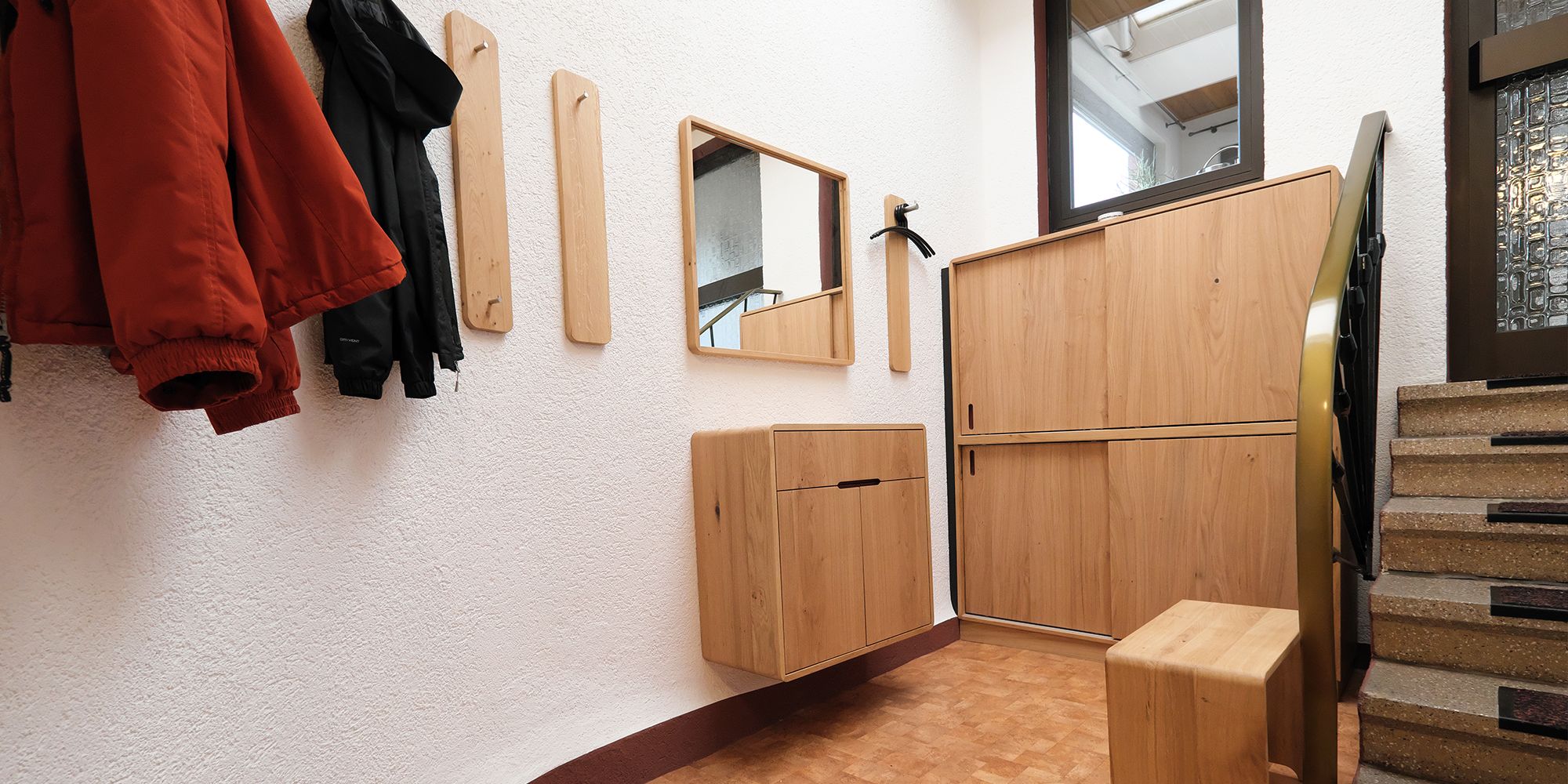 Hausflur mit Eichenholz-Garderobe, Wandhaken, Spiegel und schwebendem Sideboard neben der Treppe