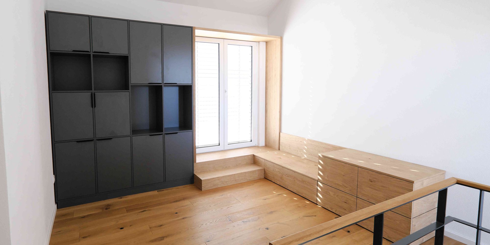 Galerie mit schwarzem Wandschrank und heller Eichen-Sitzbank mit Schubladen am Fenster, Treppe im Vordergrund