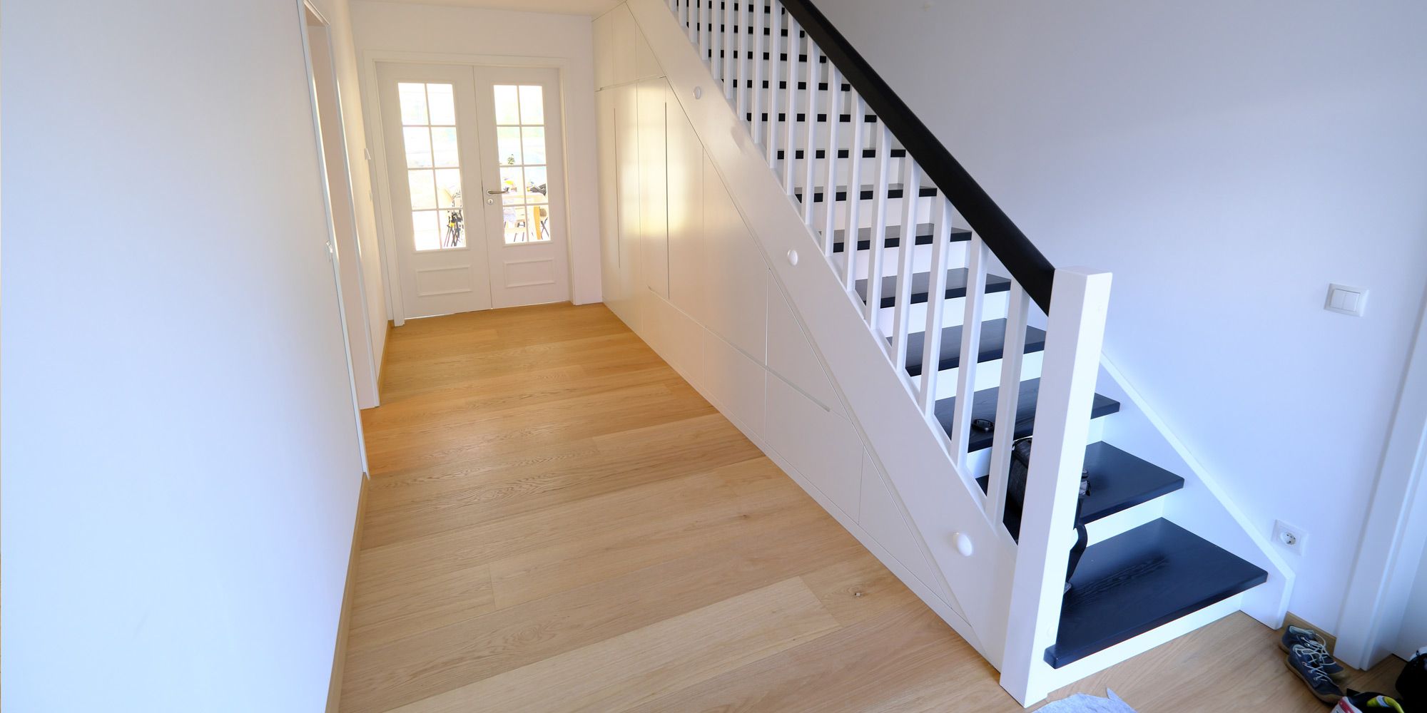 Weißlackierter Einbauschrank unter der Treppe im Flur mit Eichenparkett und schwarzen Treppenstufen