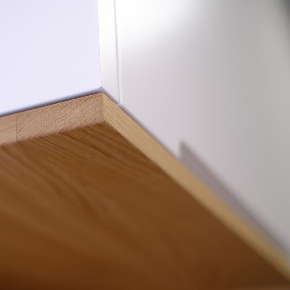 Detailaufnahme präziser Gehrung zwischen weißlackierter Schrankfront und Eichenholz-Sockelleiste