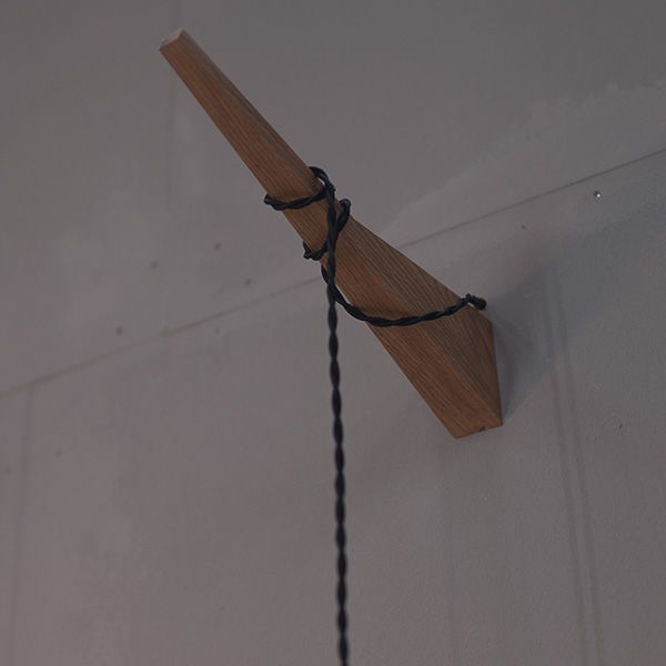 Keilförmige Massivholz-Wandhalterung der Leuchte Fitis mit textilummanteltem Kabel im Detail