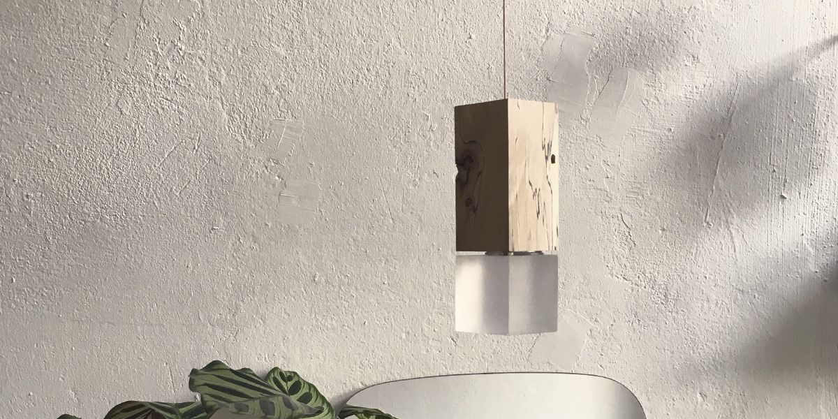 Pendelleuchte Zilpzalp mit kantigem Holzkopf und Milchglaszylinder vor strukturierter Wand