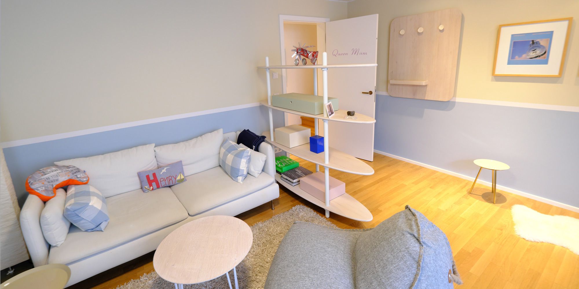 Jugendzimmer mit pastellblauer Wand, weißem Sofa und offenem Raumtrenner-Regal in Surfboard-Optik