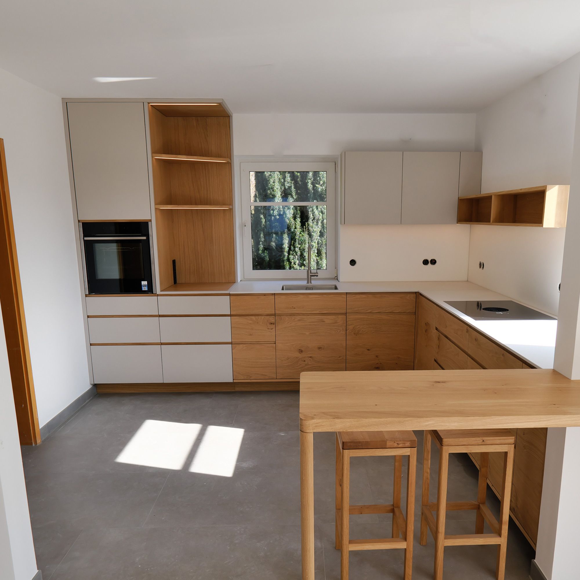 Moderne Küche in Eiche mit grauen Oberschränken, offenem Regal und Theke mit Barhockern