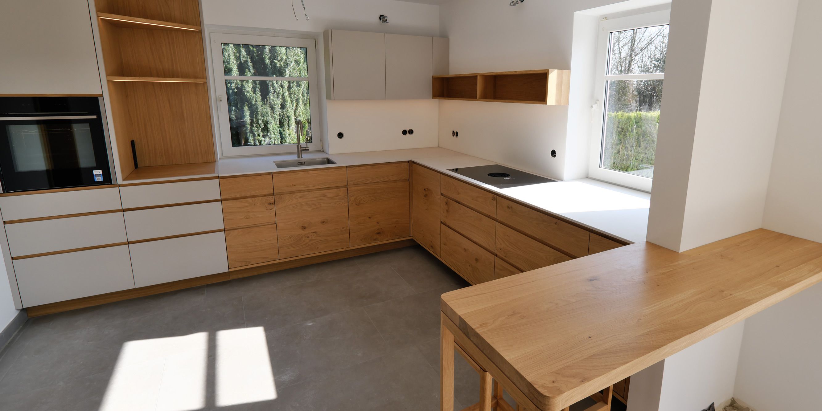 Weitwinkelansicht moderner Eichenküche mit Theke, offenem Regal und viel Tageslicht