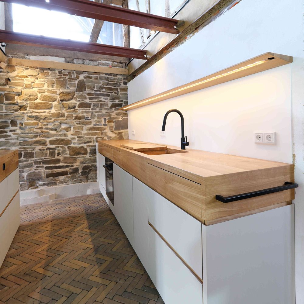 Küchenzeile mit Eichenholz-Arbeitsplatte und Holzspüle unter Lichthof mit Natursteinwand