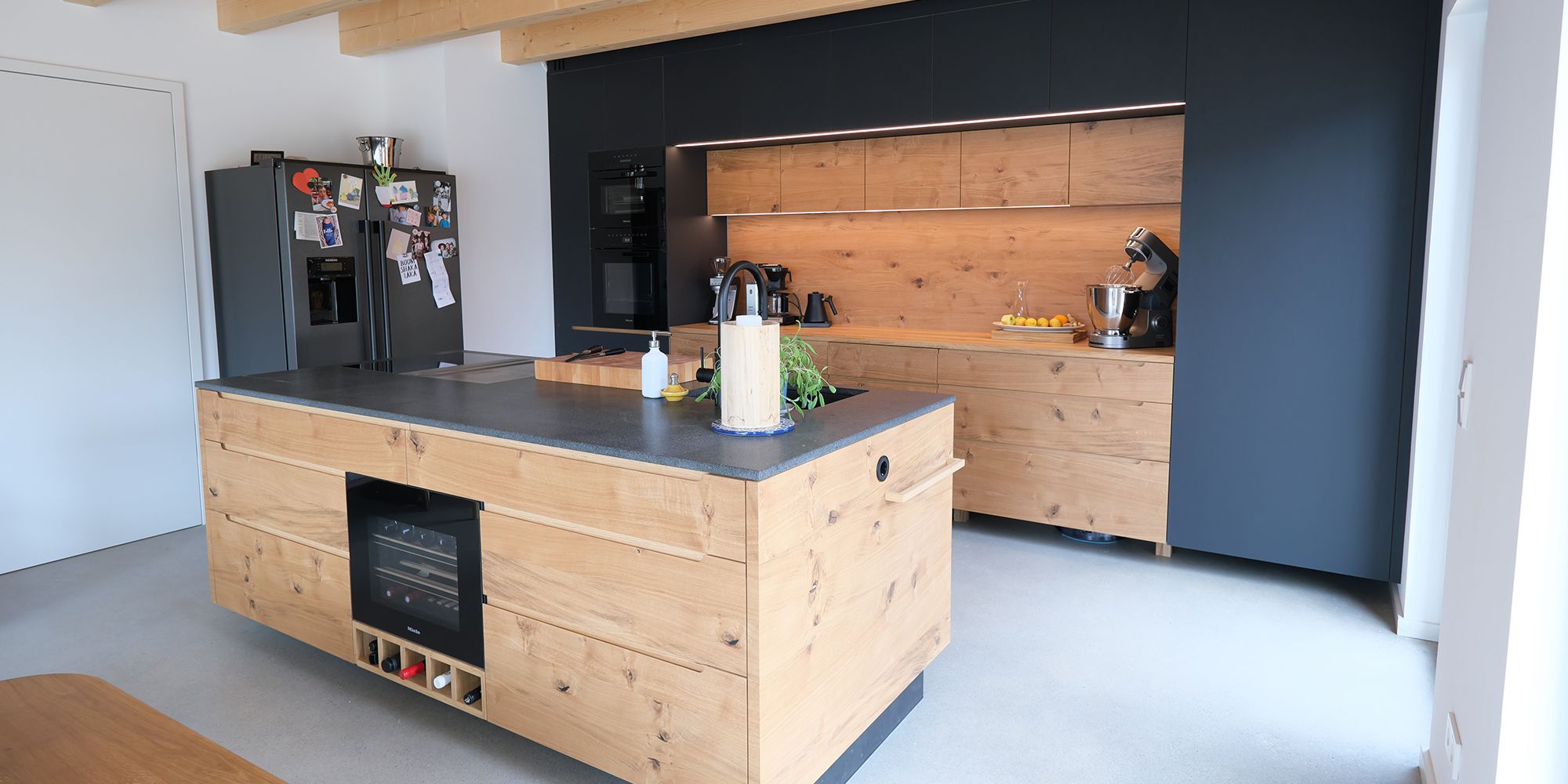 Eichenküche mit Kochinsel, integriertem Weinkühlschrank, dunkler Arbeitsplatte und sichtbarer Holzbalkendecke