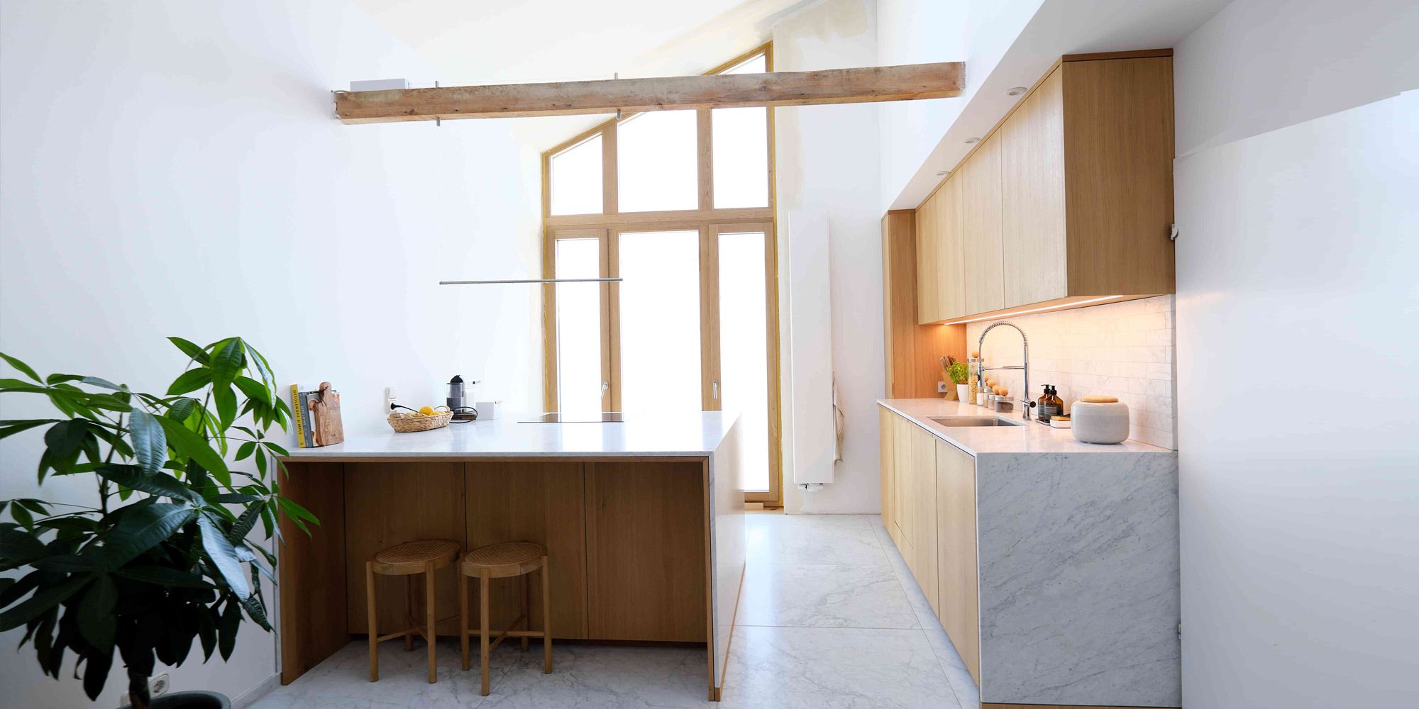 Helle Eichenküche mit Marmor-Arbeitsplatte und Kochinsel in lichtdurchflutetem Altbau mit Holzbalken