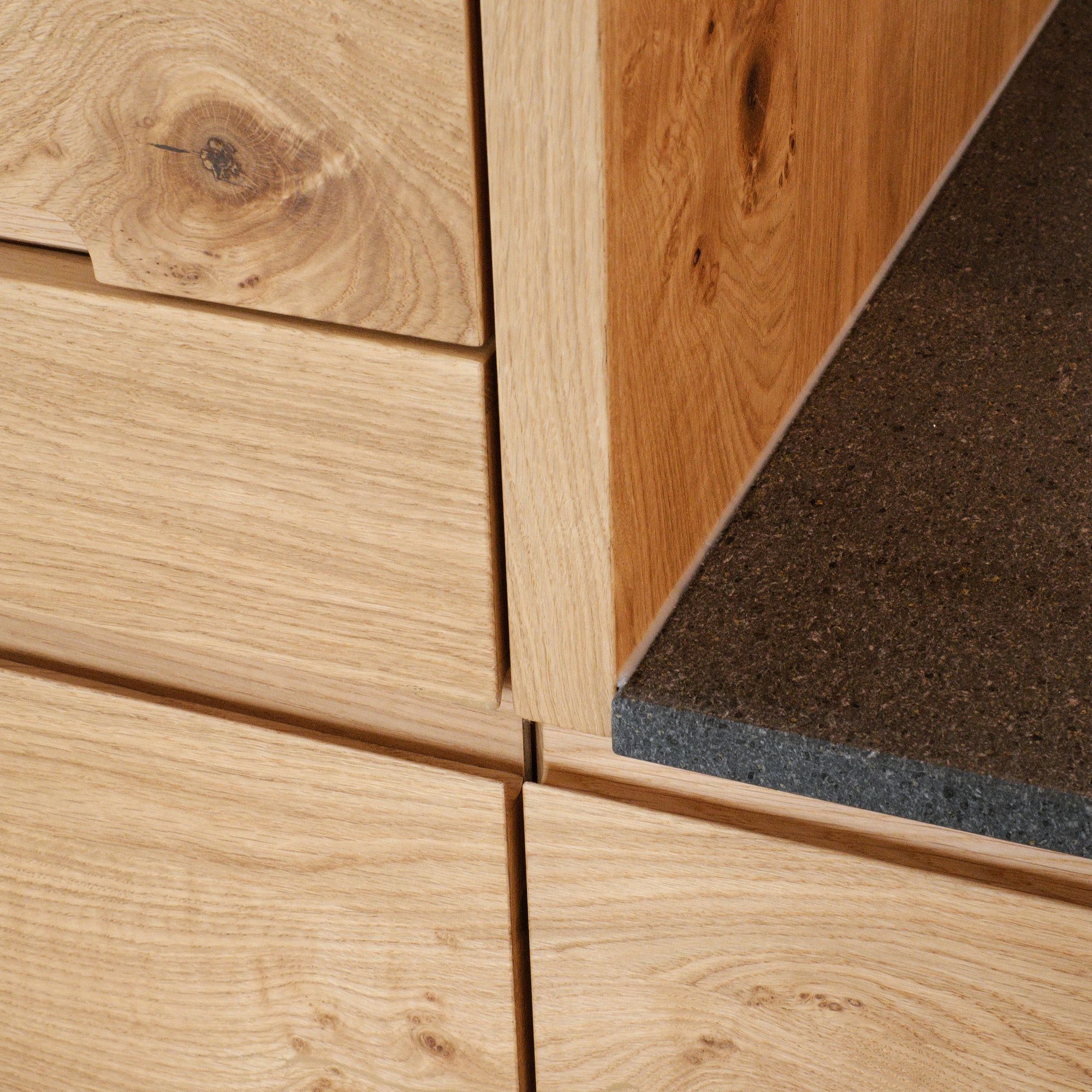 Detailaufnahme Eichenholz-Schubladen mit Astloch neben dunkler Naturstein-Arbeitsplatte