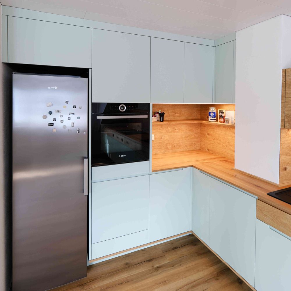 Pastellgruene Kueche mit Edelstahlkuhlschrank, offenem LED-Regal und Eichenholz-Arbeitsplatte