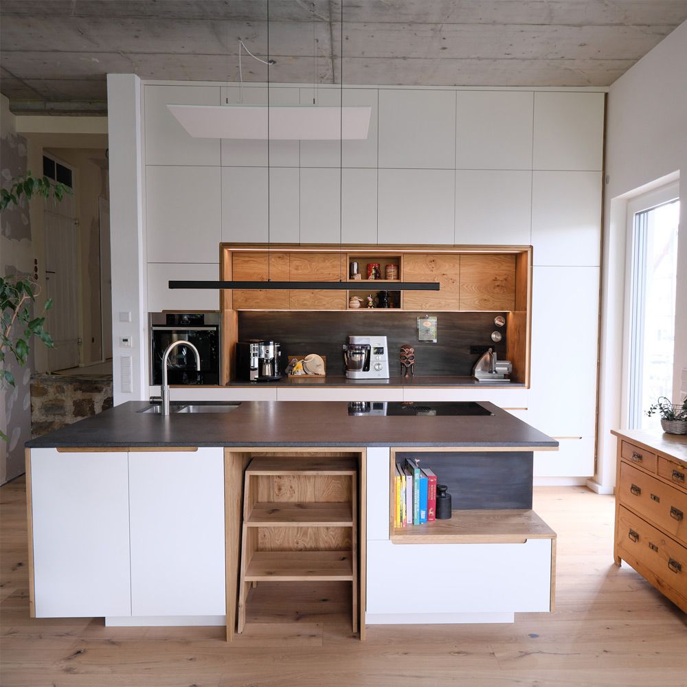 Kochinsel mit weißen Fronten, Eiche-Regalwand und Natursteinplatte unter Betondecke im Loft