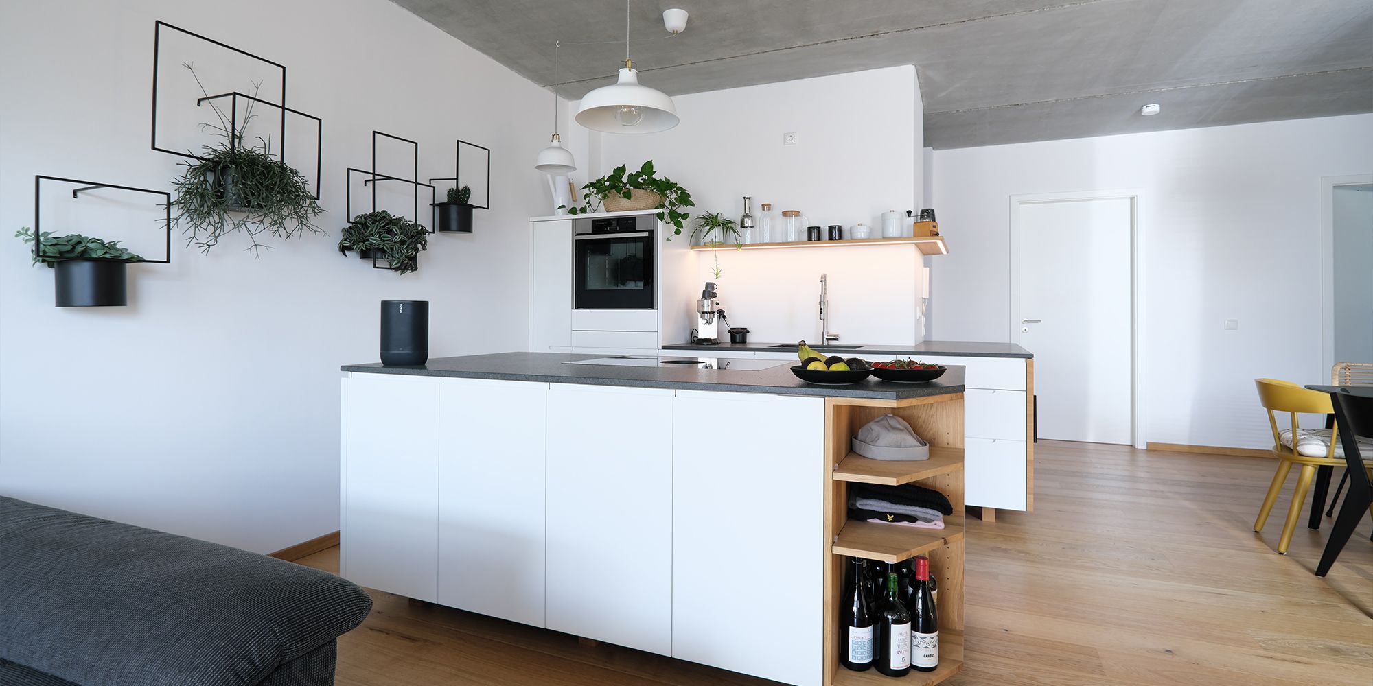 Weiße Küche mit Kochinsel, Eichenregal und Steinarbeitsplatte in offenem Loft-Wohnraum