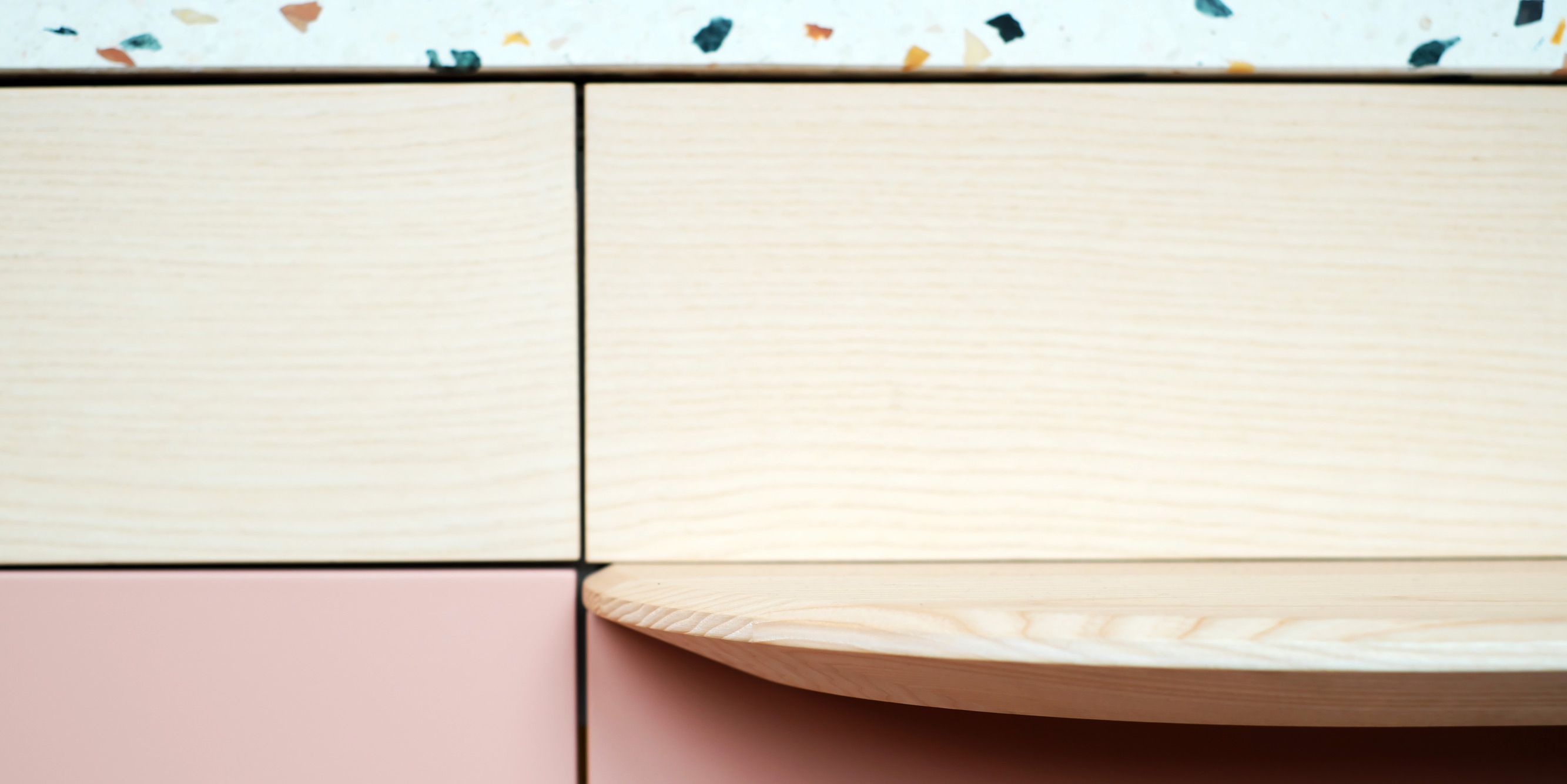 Nahaufnahme der abgerundeten Esche-Massivholzkante mit Terrazzo-Arbeitsplatte und rosa Lackfront