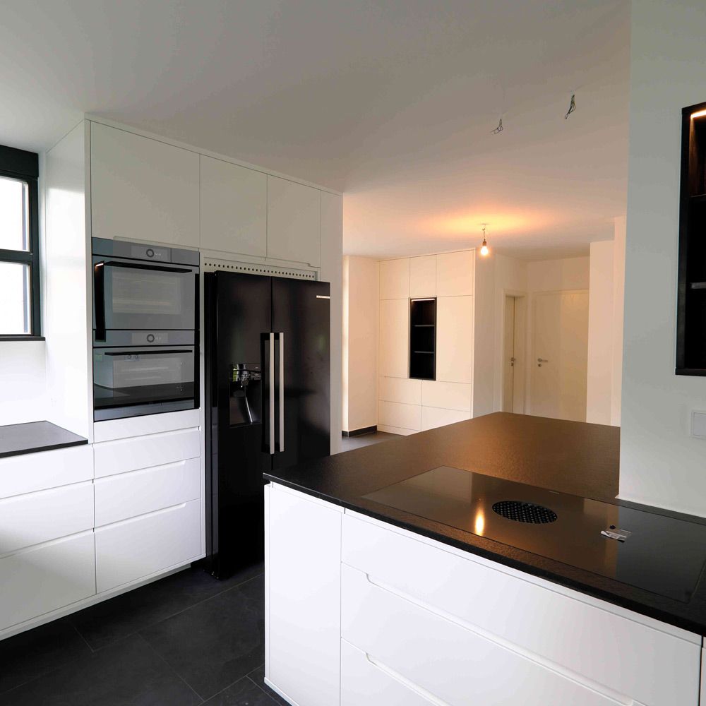 Weiße Hochglanzküche mit schwarzem Side-by-Side-Kühlschrank und Natursteintheke im offenen Wohnraum