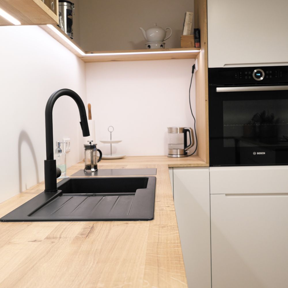 Moderne Küche mit Eiche-Arbeitsplatte, schwarzer Spüle und Armatur, weißen Fronten und LED-Beleuchtung