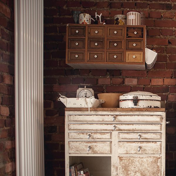 Vintage-Deko mit altem Apothekerschrank und rustikaler Kommode vor Ziegelwand im Landhausstil