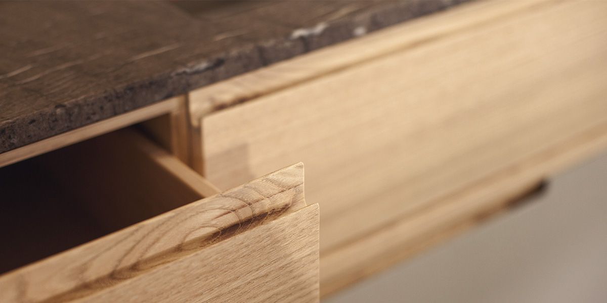Geöffnete Massivholzschublade mit Griffmulde unter dunkler Steinarbeitsplatte im Detail