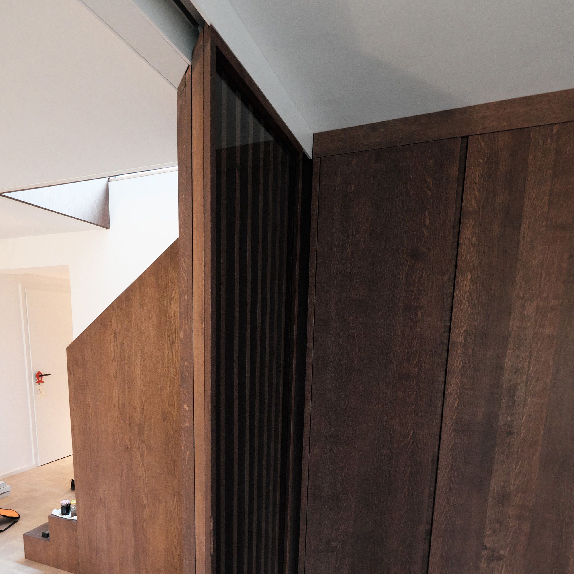 Treppenverkleidung mit Lamellenwand und Glasschiebetür aus dunkel geöltem Massivholz in Montage