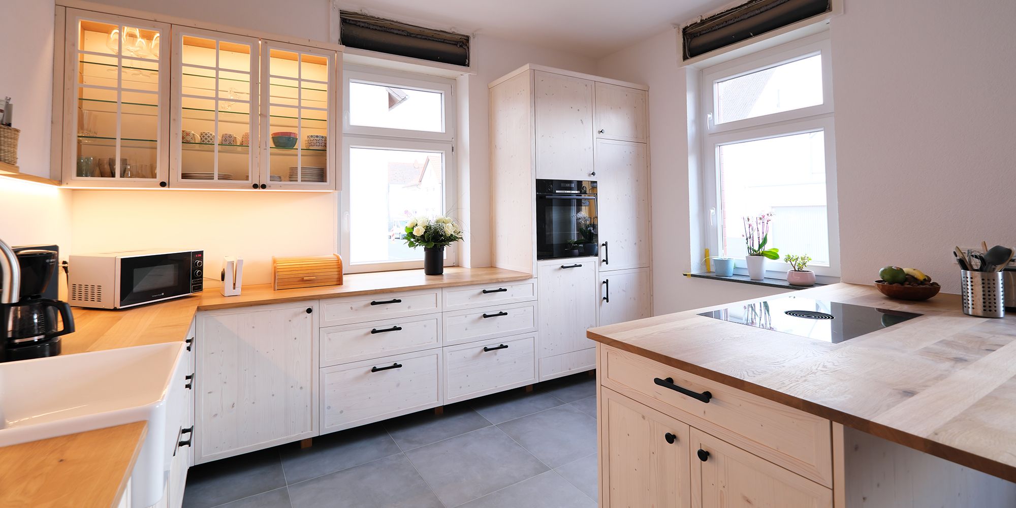 Landhausküche aus weiß geölter Fichte mit Glasvitrine, schwarzen Metallgriffen und Kücheninsel