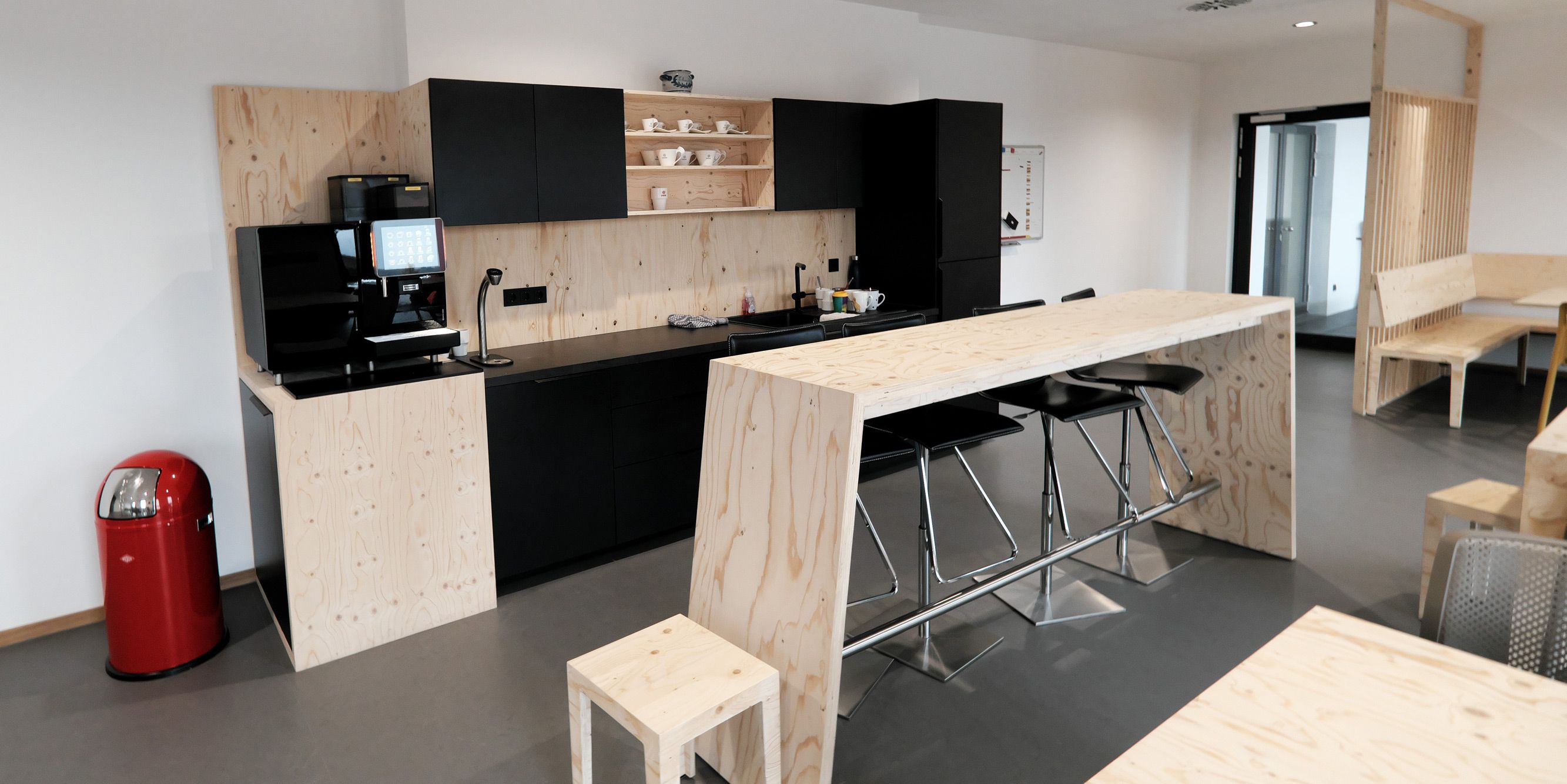 Pausenraum mit Seekiefer-Sperrholz-Theke, schwarzer Küchenzeile und Stehtisch mit Barhockern