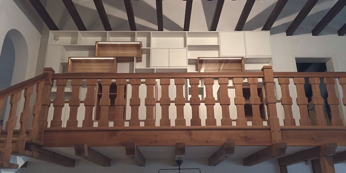 Empore mit klassischer Holzbalustrade und dahinterliegendem Weißlack-Regalsystem mit Eiche-Vitrinen unter Dachbalken