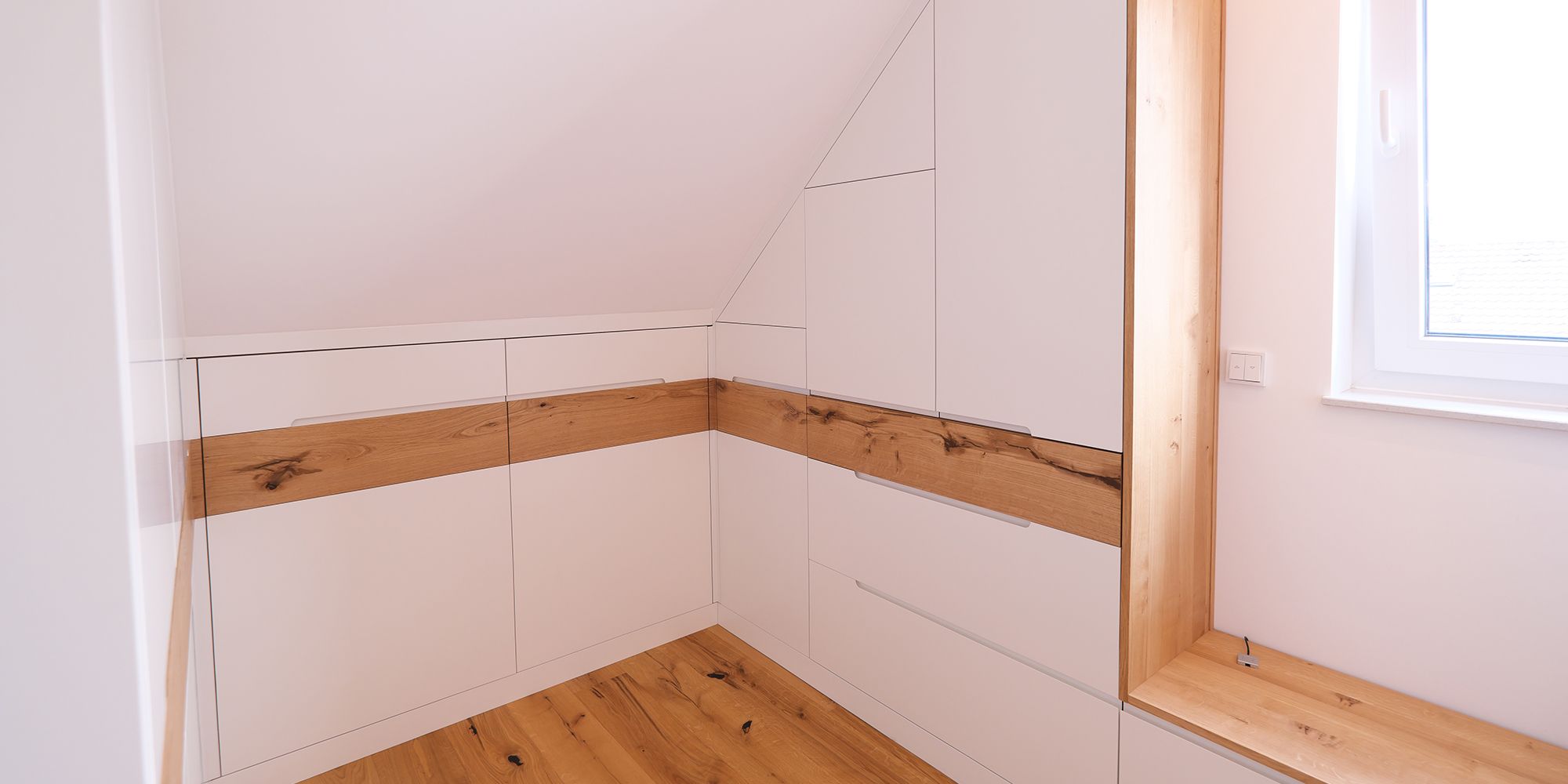 Weißer Dachschrägenschrank mit Eichenholz-Griffleiste und Fensterlaibung aus Massivholz im Schlafzimmer