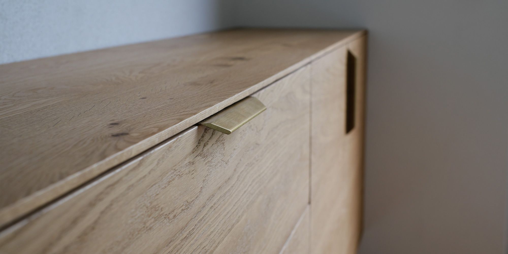Nahaufnahme eines Messing-Kantengriffs an einem Eiche-Sideboard mit sichtbarer Holzmaserung