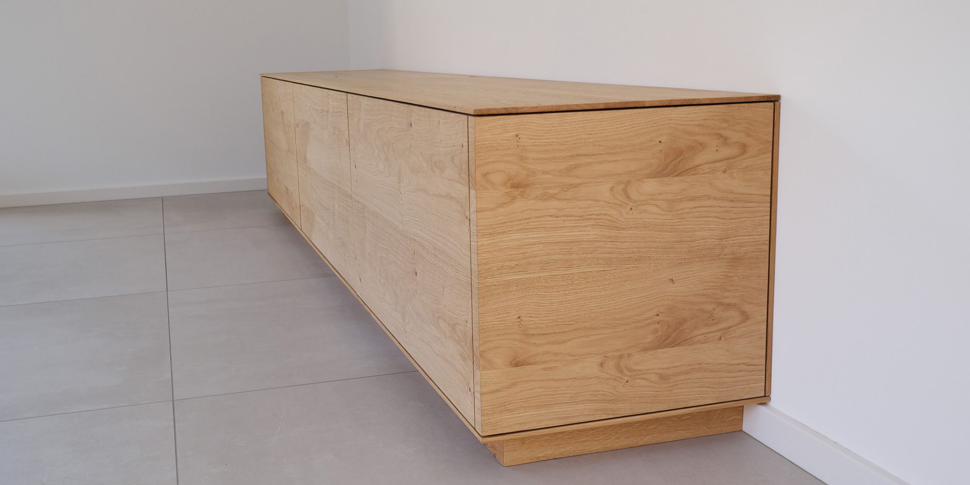 Filigranes Eiche-Sideboard mit lebhafter Maserung auf hellem Fliesenboden in Zimmerecke