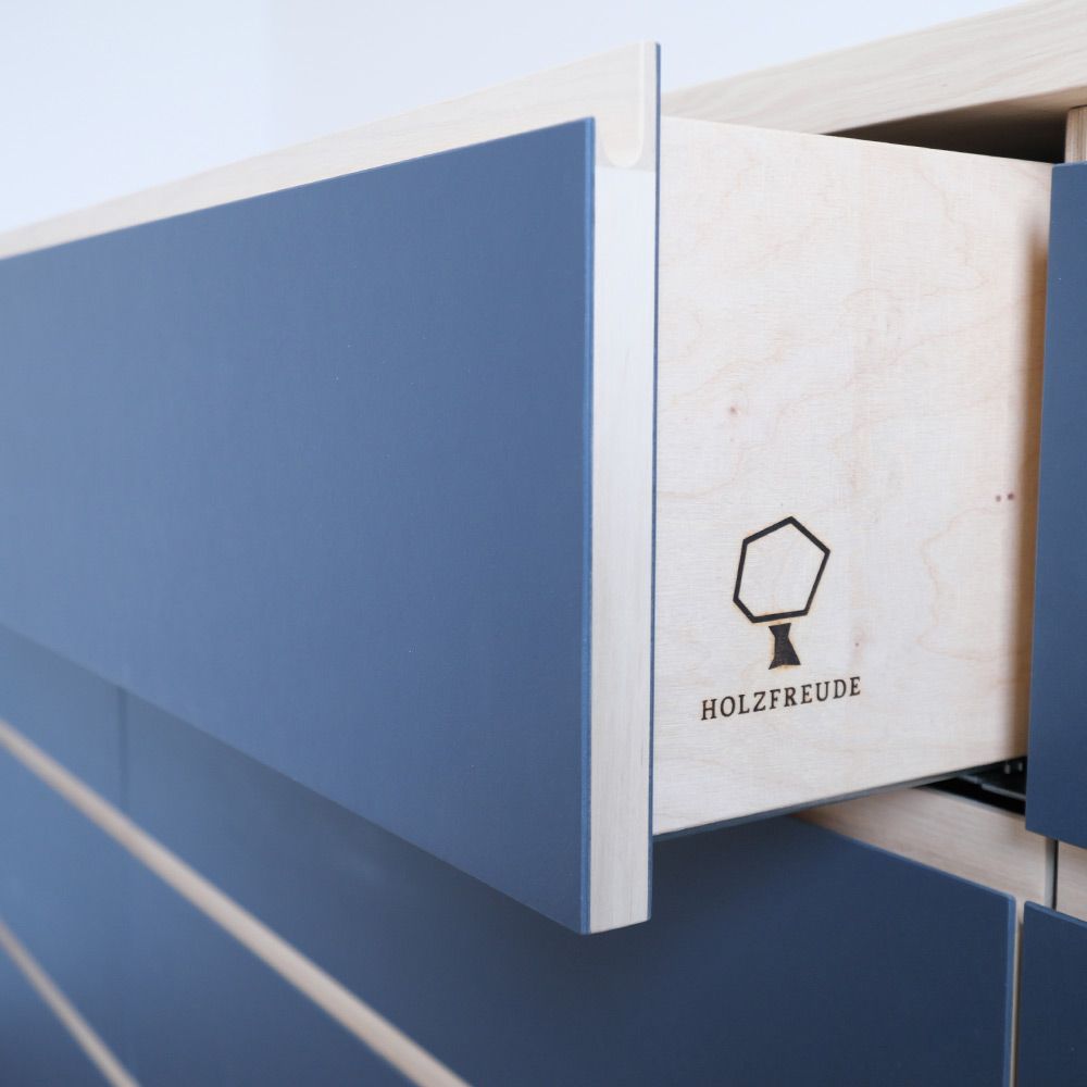 Geöffnete Schublade mit eingebranntem Holzfreude-Logo auf Hainbuche-Holz, blaue Linoleumfront