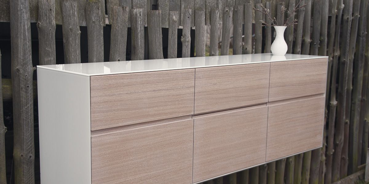 Grifflos wandhängendes Sideboard mit weißer Seitenwange, Diagonalansicht vor Holzzaun mit Vase
