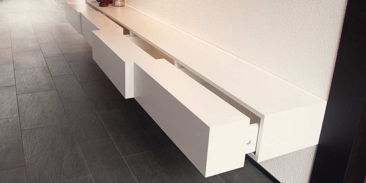 Schwebendes weißes Sideboard mit grifflosen Schubladen auf dunklem Fliesenboden