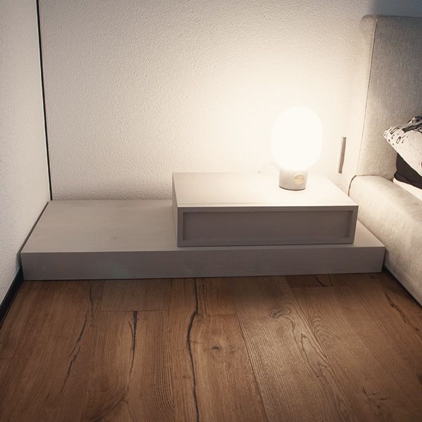 Weißes Podestmöbel mit integrierter Ablage und Tischlampe neben Sofa auf Holzdielenboden
