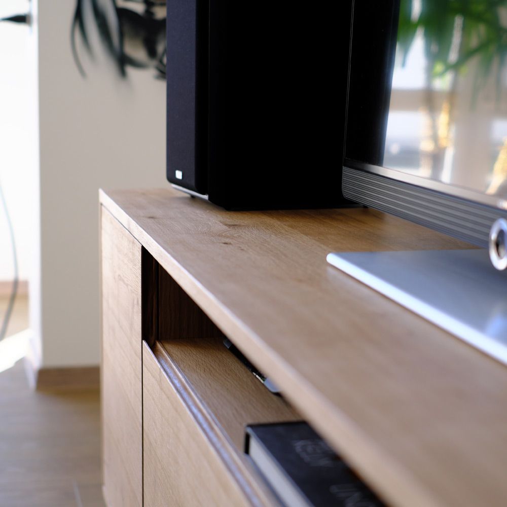 Nahaufnahme der geölten Eiche-Oberfläche eines TV-Sideboards mit offener Schublade und Lautsprecher