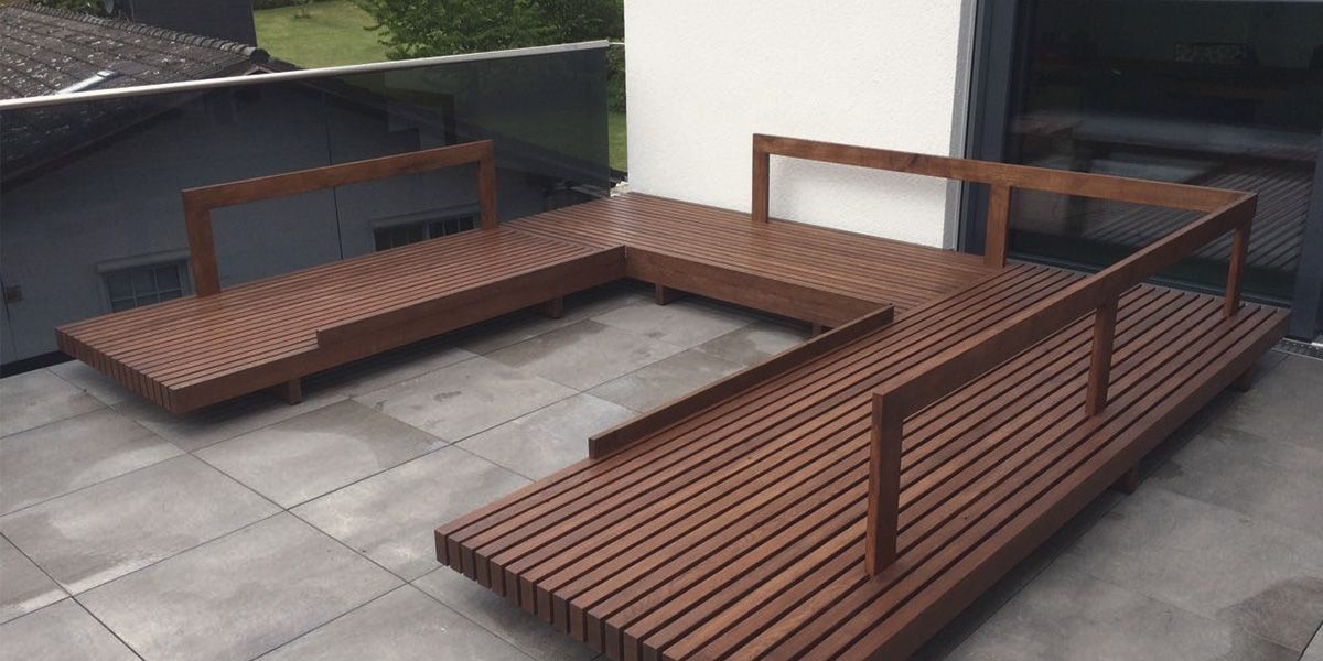 U-förmige Terrassen-Loungebank aus dunkel gebeiztem Lamellenholz auf einer Dachterrasse