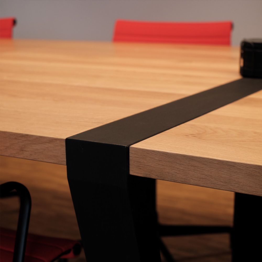 Konferenztisch aus Eiche Massivholz mit schwarzem Metallgestell im Detail, rote Stühle im Hintergrund