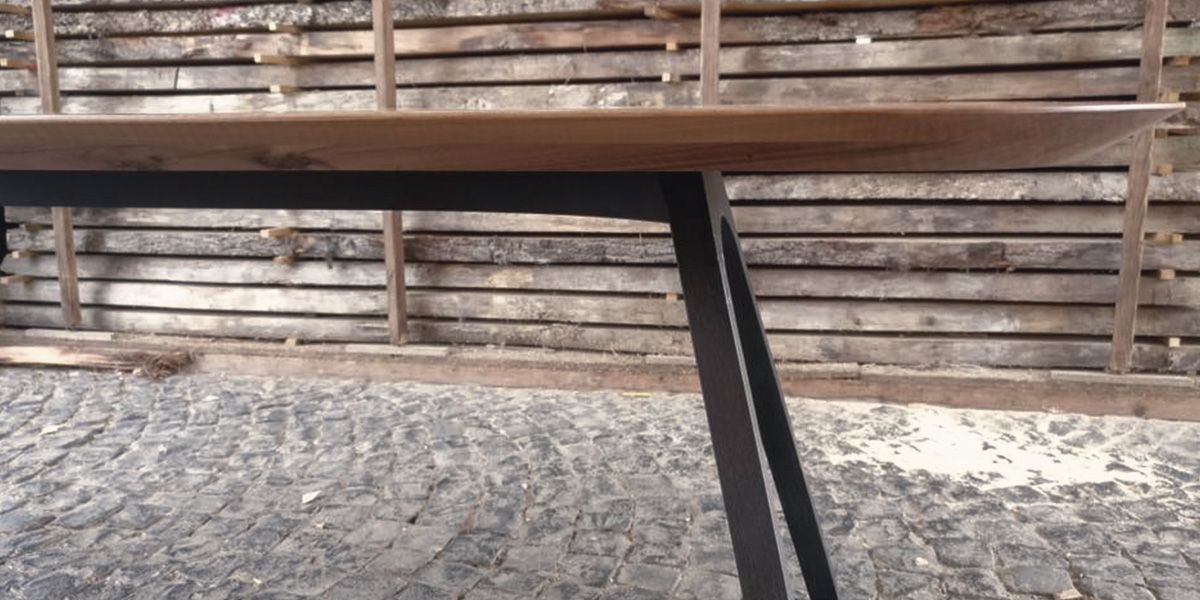 Tisch aus Nussbaumholz mit schlankem schwarzem Stahlgestell im Außenbereich vor Holzstapel