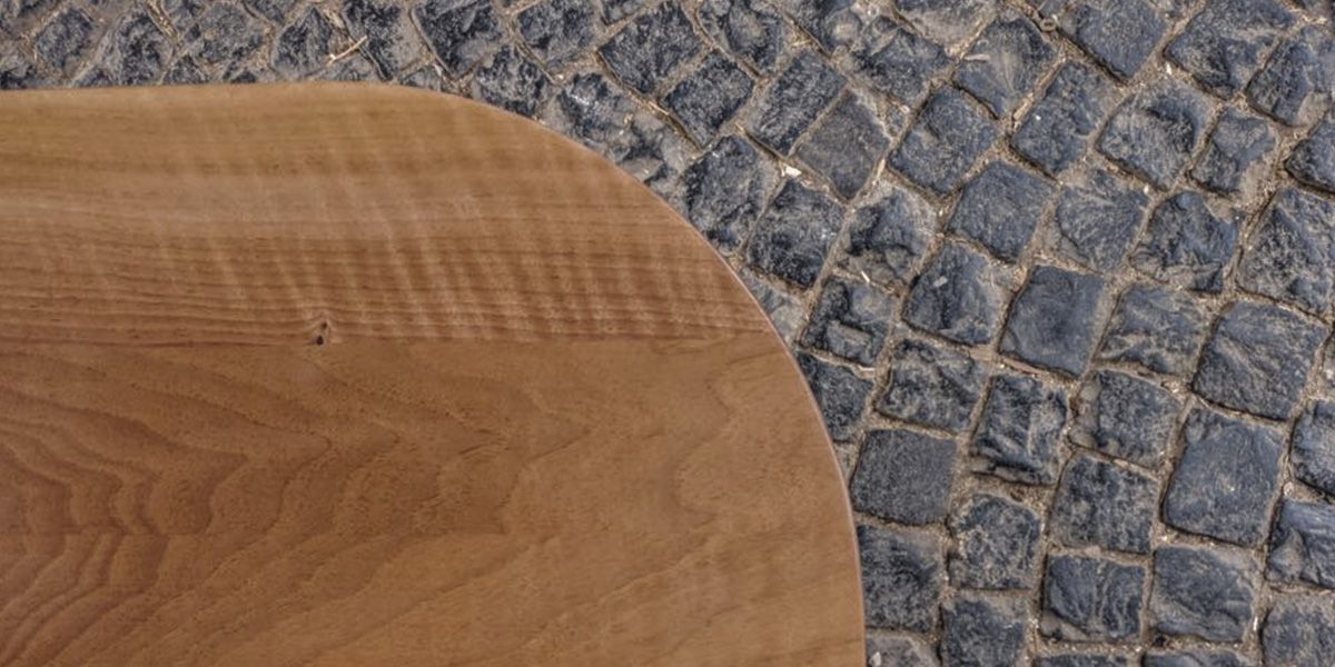 Runde Tischplatte aus massivem Nussbaumholz mit sichtbarer Maserung auf Kopfsteinpflaster